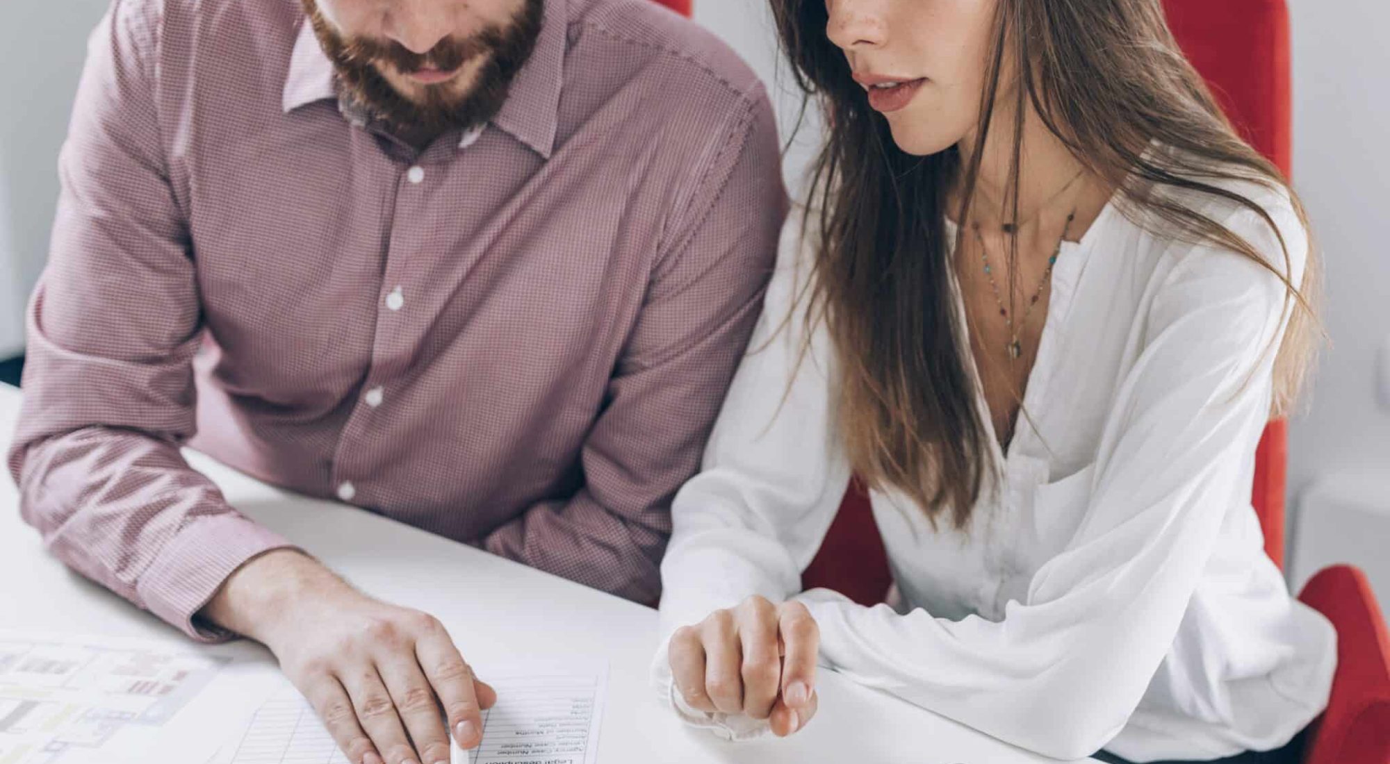 Two people sit at a table reviewing documents together, both pointing at the papers, with a smartphone placed nearby.